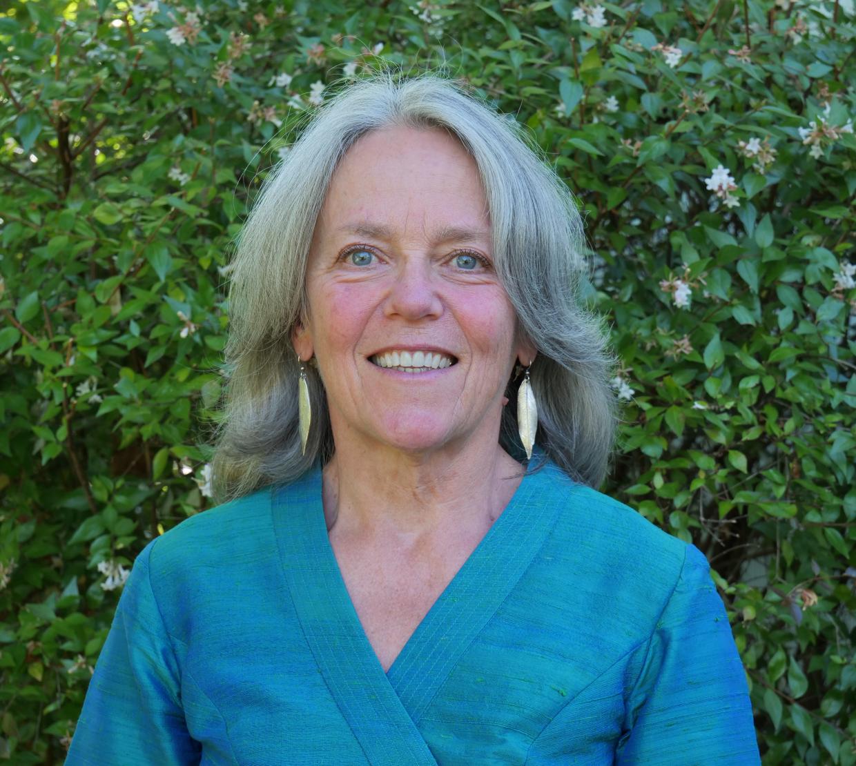 Manuela Huso in a blue shirt in front of green bushes.