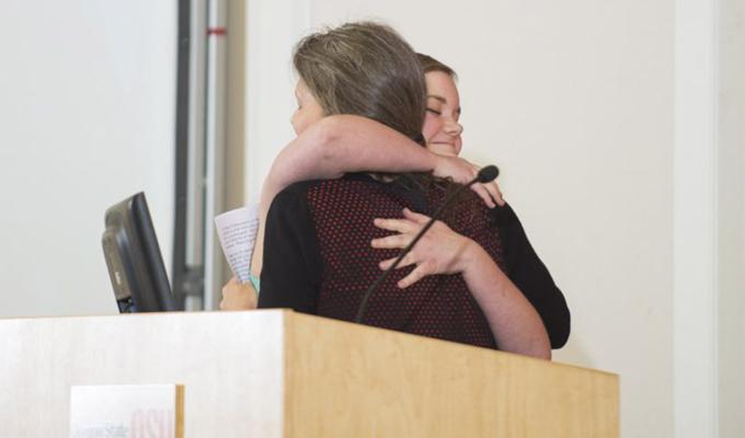 Two women hugging each other behind podium