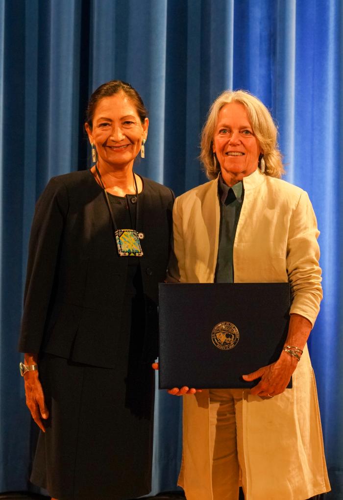 Two women in professional attire in front of a blue background.